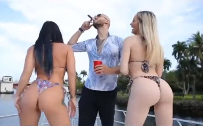 He appears to be smoking a cigar flanked by women in bikinis