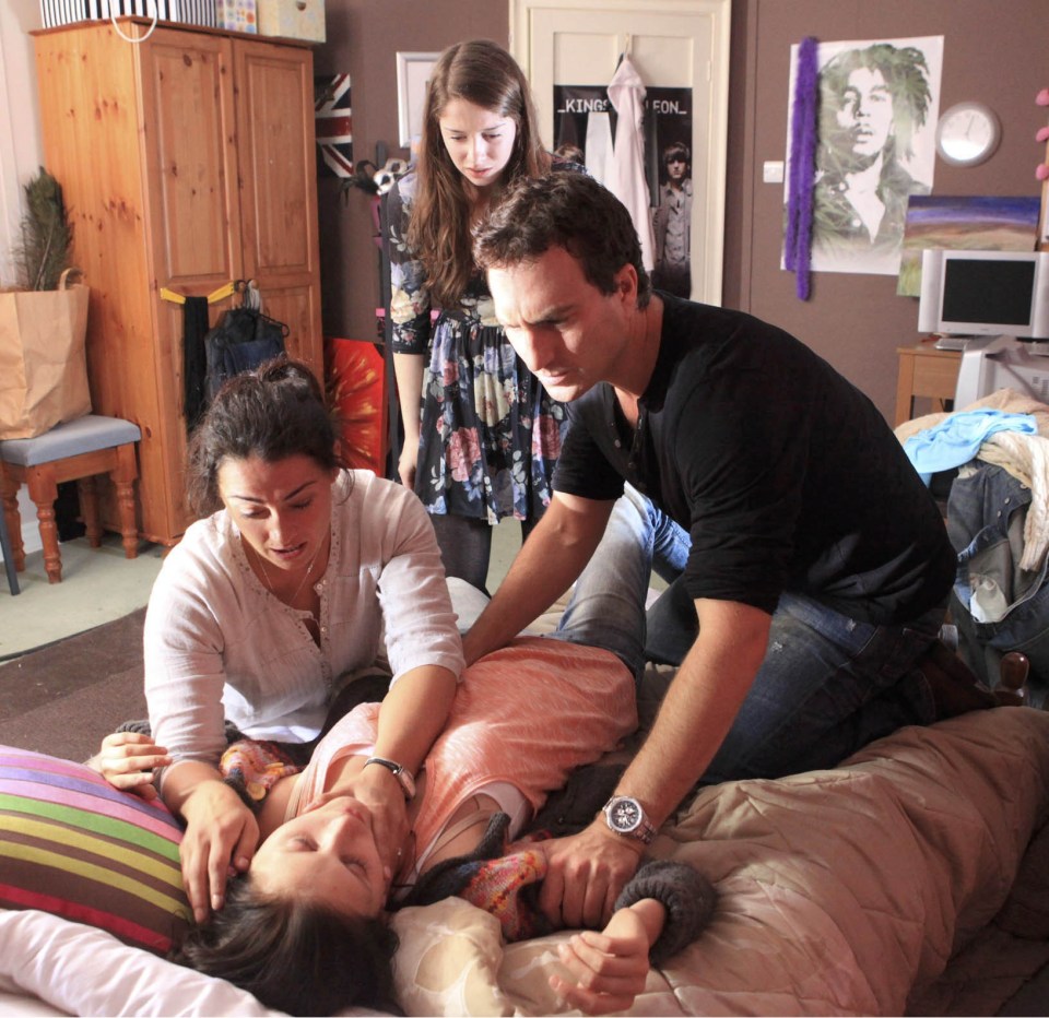 Screenshot from the TV show *Emmerdale* depicting three characters reacting to a fourth character who is overdosing on heroin.