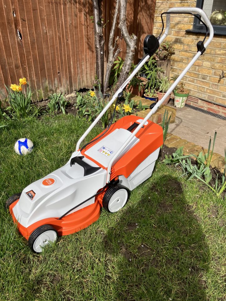Orange and white electric lawnmower on a lawn.