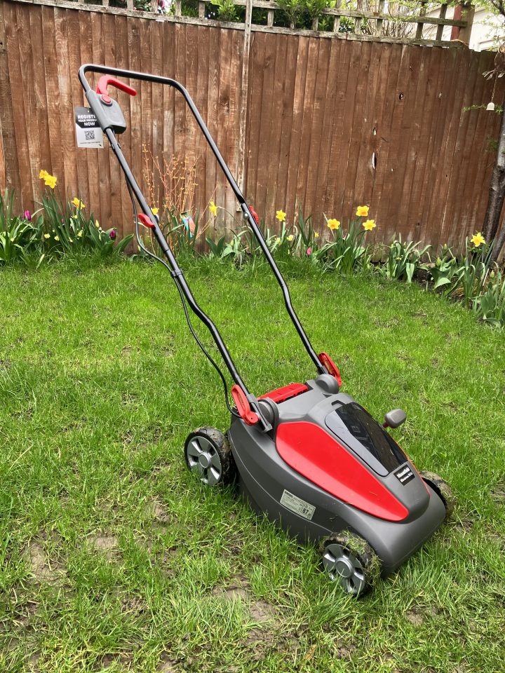 Red and gray electric lawnmower on a grassy lawn.