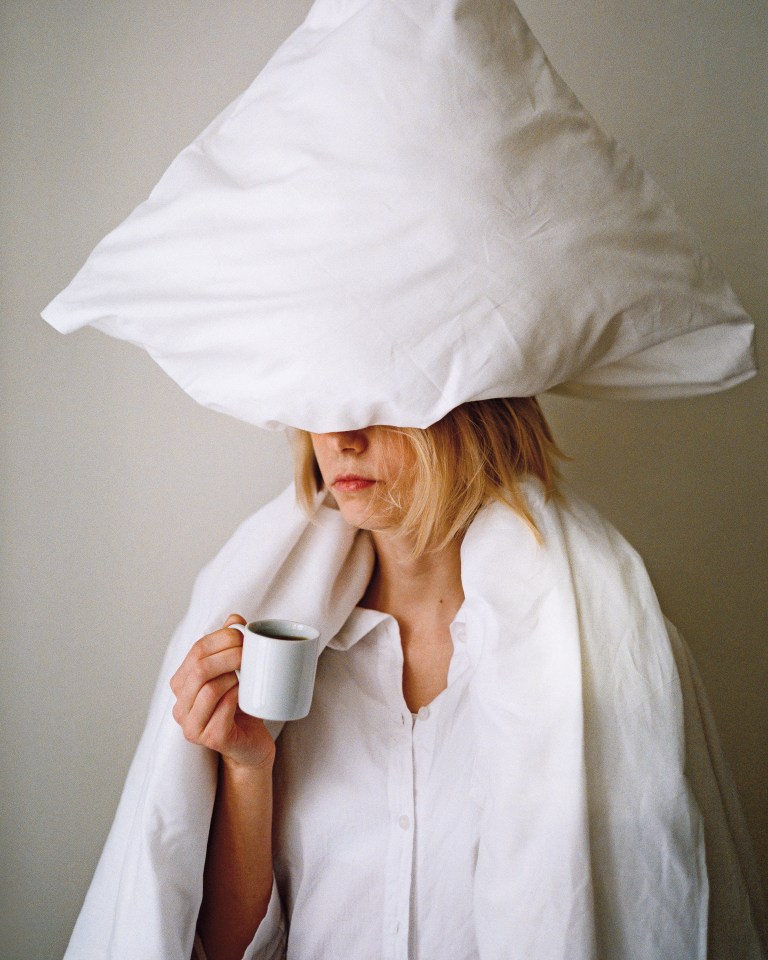 a woman with a pillow on her head drinking a cup of coffee