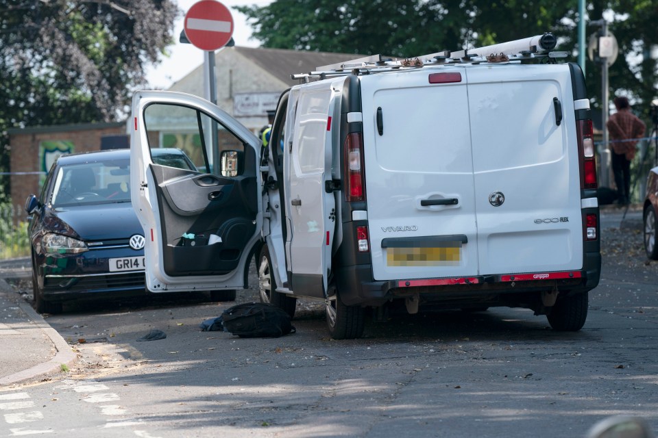 A rucksack and other items are pictured on the road next to the open door of a white van