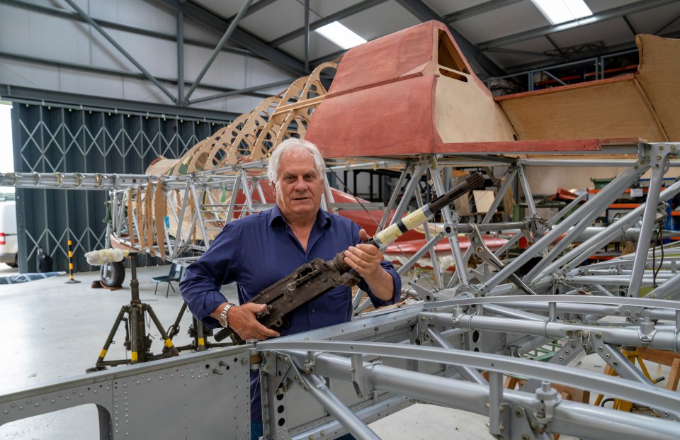 Man holding a machine gun in front of a plane reconstruction.