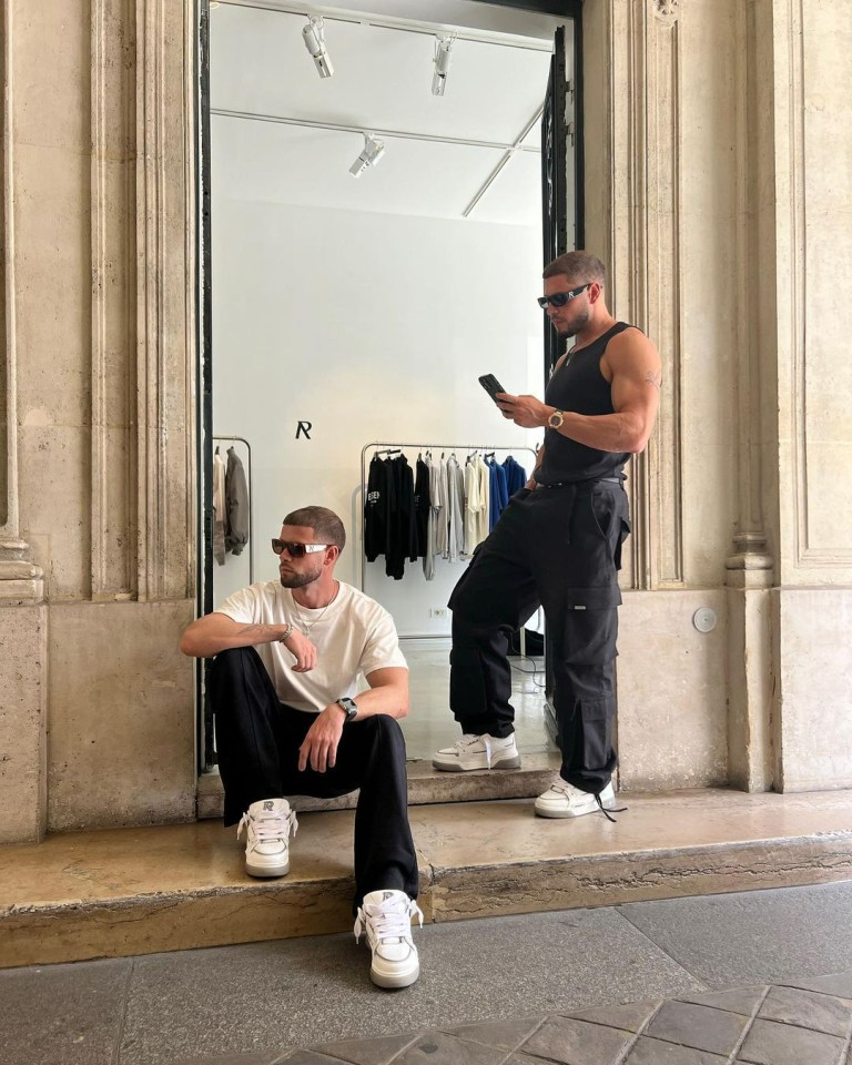 Two men in sunglasses and casual attire sitting outside a store.