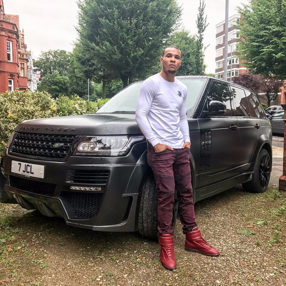 Man in white long-sleeve shirt and burgundy pants standing next to a black Range Rover.