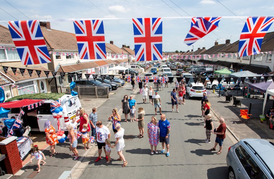 Street party with residents celebrating, decorated with Union Jack flags.