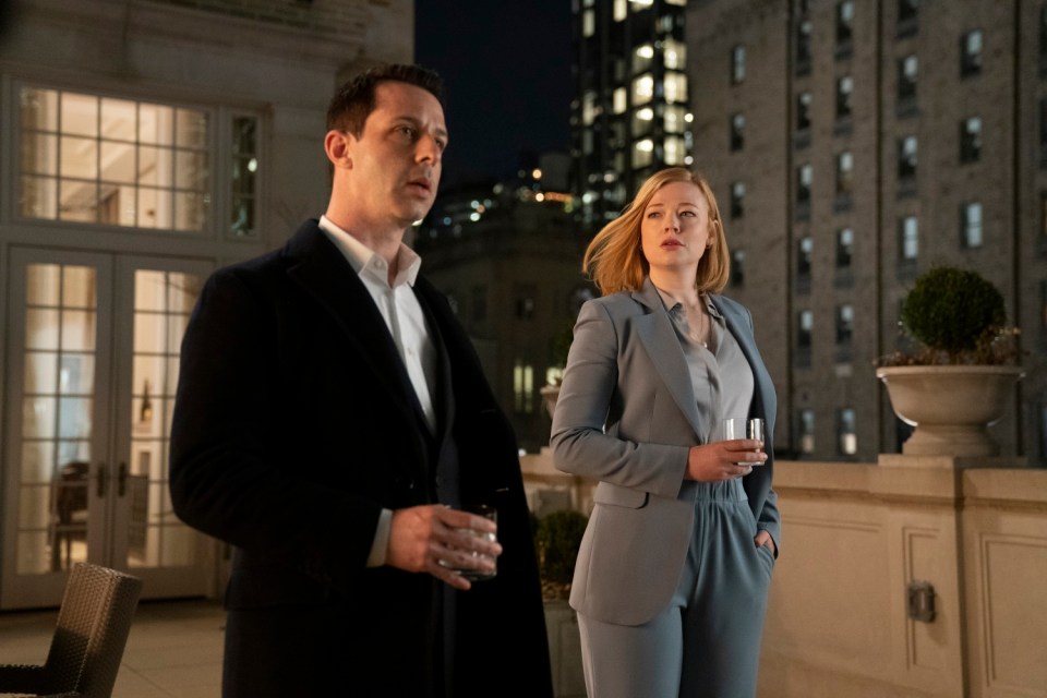 A still from Succession season 2 showing two characters, a man and a woman, standing on a balcony at night.