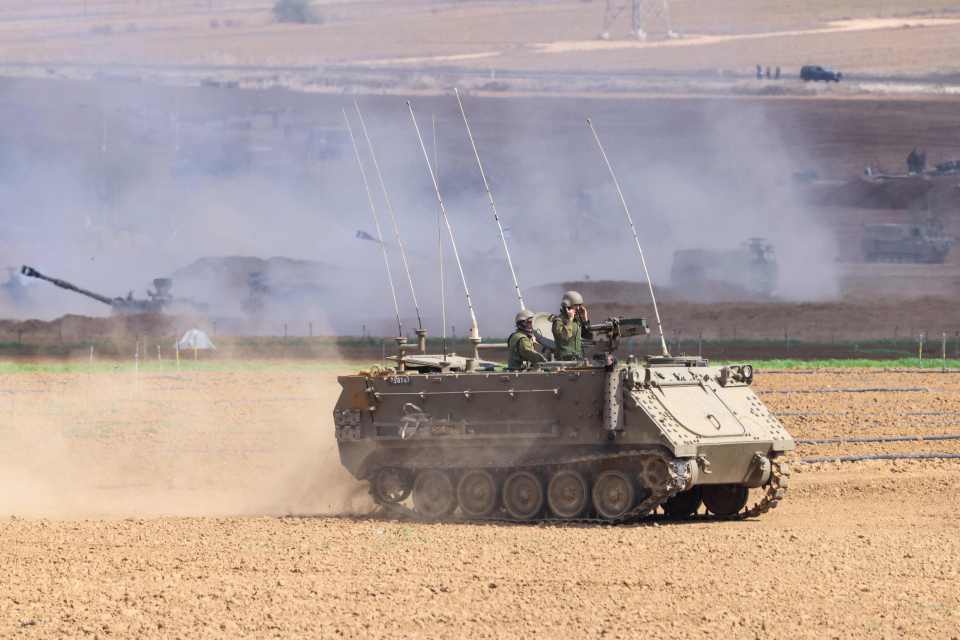 Israeli soldiers man an armoured vehicle as they fire artillery cannon towards the Gaza Strip