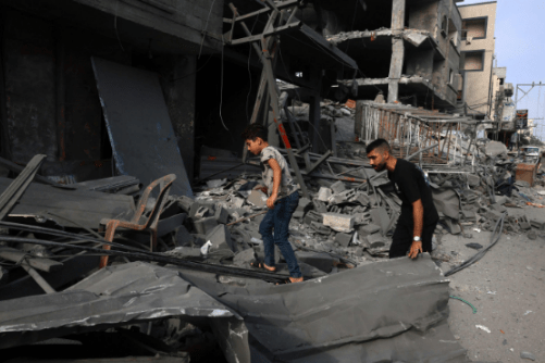People check the wreckage of a destroyed building after bombings in the Strip