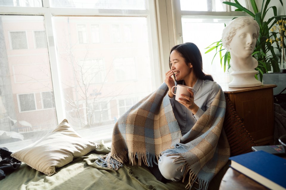 a woman wrapped in a plaid blanket holds a cup of coffee