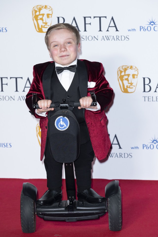 a young boy in a suit stands in front of balloons