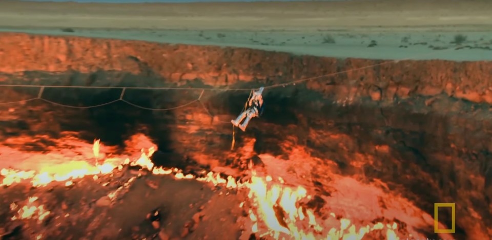 a man is hanging from a rope over a volcano