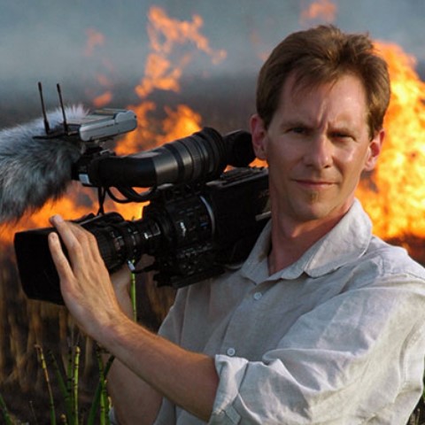 a man holding a camera in front of a fire