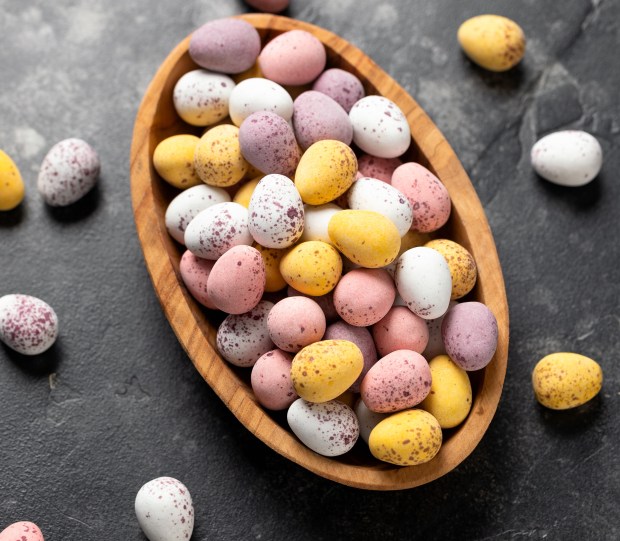 Pastel-colored chocolate Easter eggs in a wooden bowl.