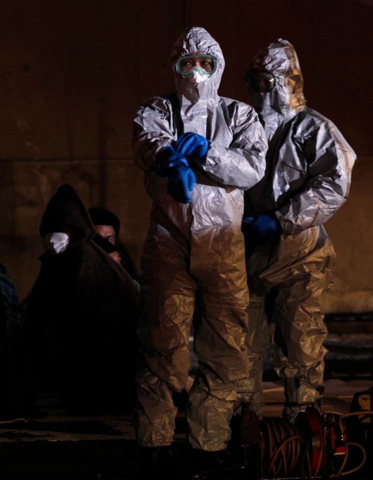 Officials in protective gear stand next to people from the evacuation area in the wake of the disaster