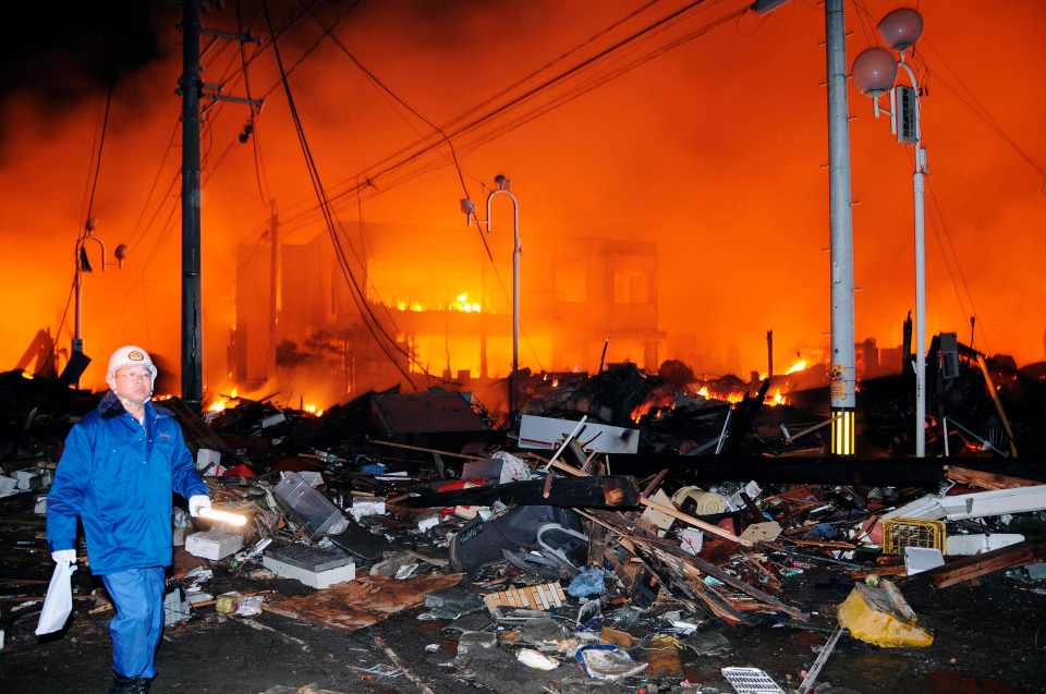 A man walks past burning rubble the day the earthquake hit Fukushima