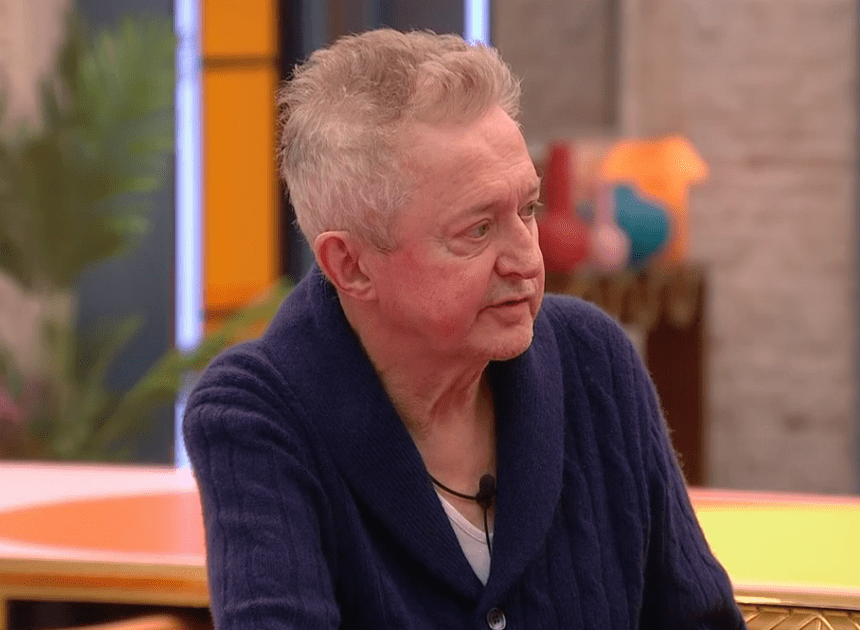 A man in a dark blue cardigan speaks.