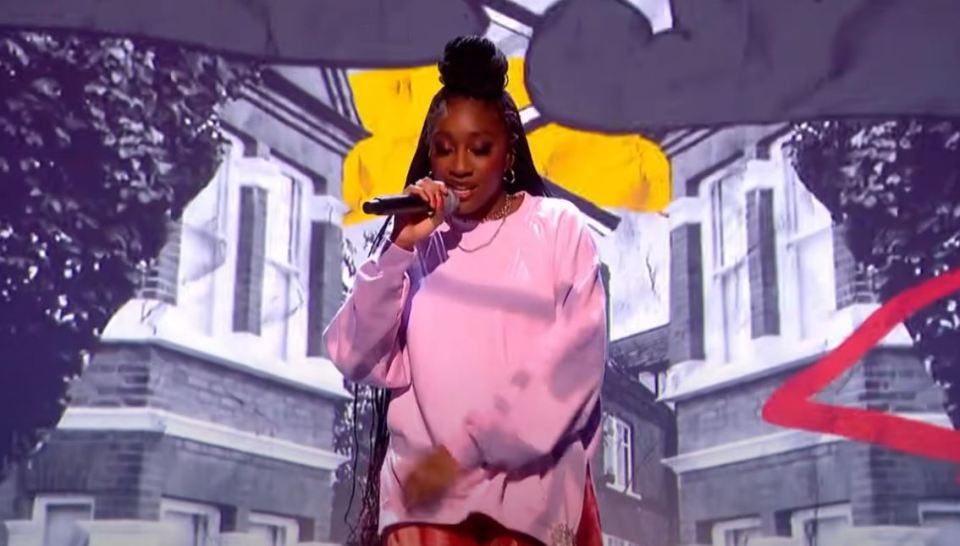 a woman in a pink sweatshirt sings into a microphone