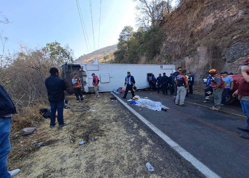 The bus lays on its side in the middle of a busy roadway