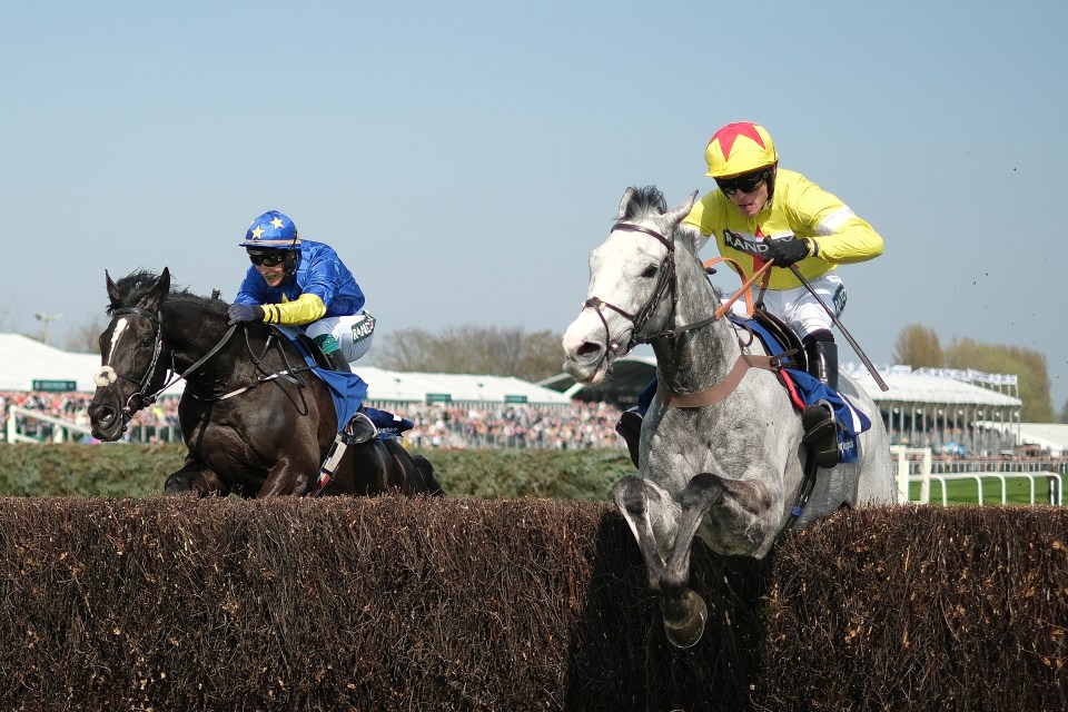 Two jockeys jump hurdles on their horses at a race.