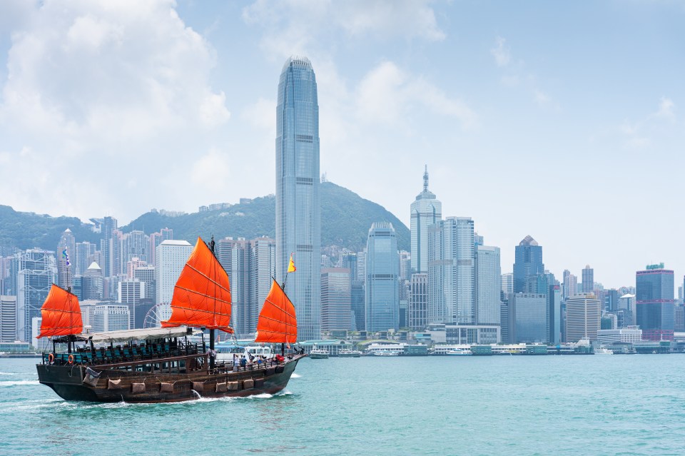 a boat with red sails is in the water in front of a city skyline