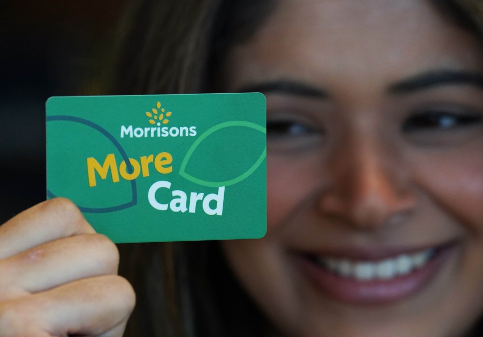 a woman holds up a green morrisons more card