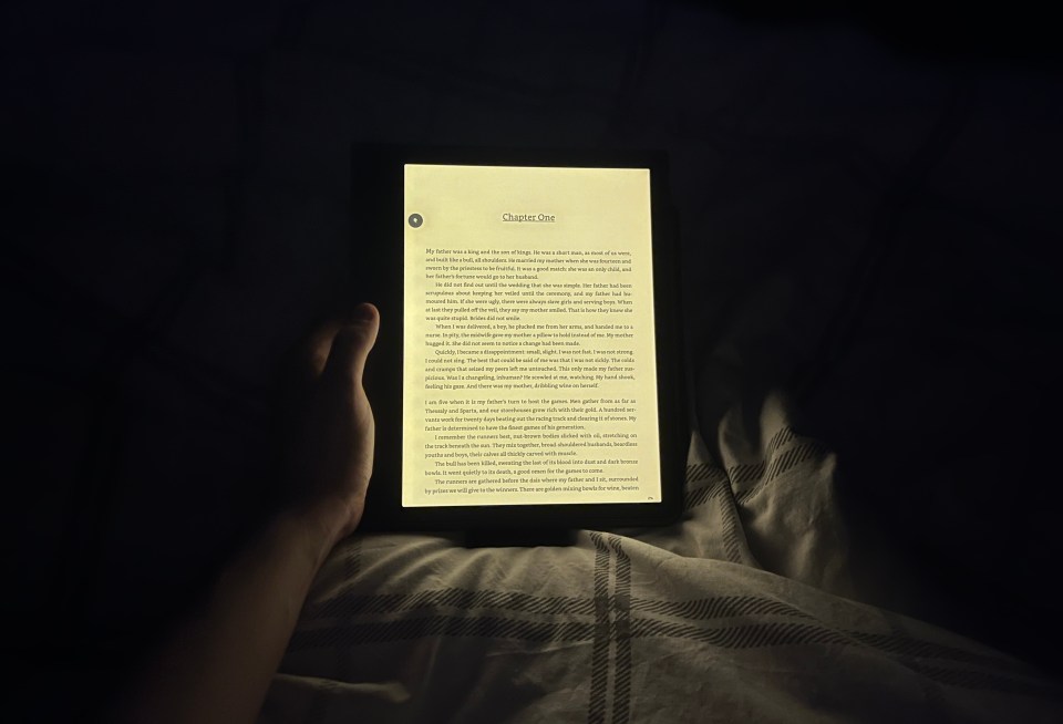 Person reading a book on an e-reader in bed at night.