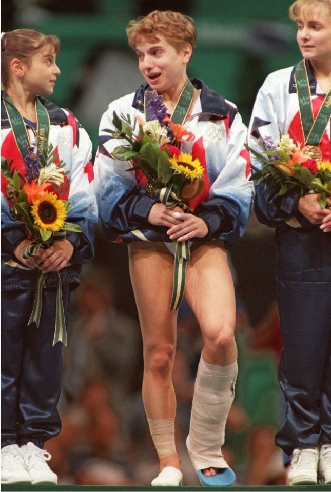 US gymnast Kerri Strug (C) with a twisted ankle wears her gold medal as she is flanked by teammates Dominique Moceanu (L) and Shannon Miller after the US won the gold in the women's gymnastic team event 23 July. (FOR EDITORIAL USE ONLY)<br />
Olympic Games; Atlanta 1996