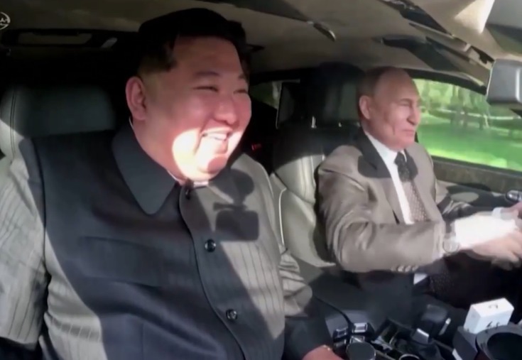 a man in a suit sits next to another man in a car