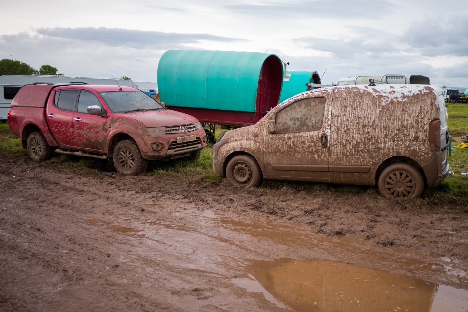 Cars parked in one of the camping fields are covered in mud on Saturday