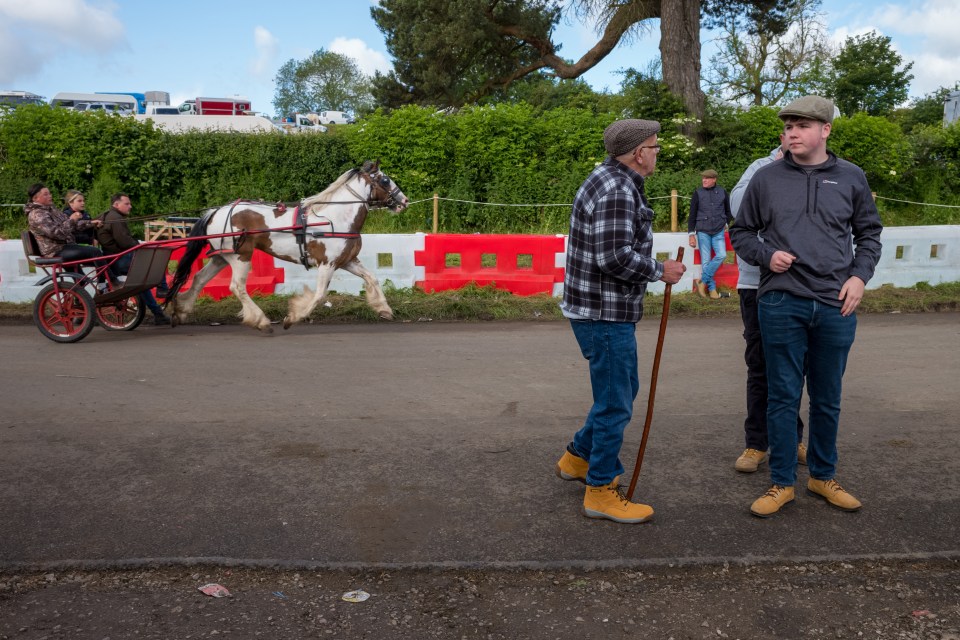 Men standing in flat caps as a horse and trailer rides by in the background on Saturday