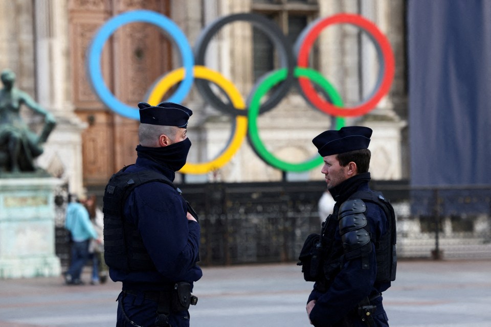French police officers stand guard, near the Olympic rings which are displayed for the Paris 2024 Summer Games