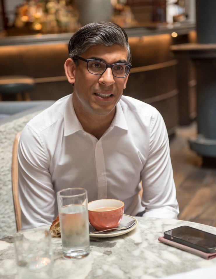 a man wearing glasses sits at a table with a cup of tea and a glass of water