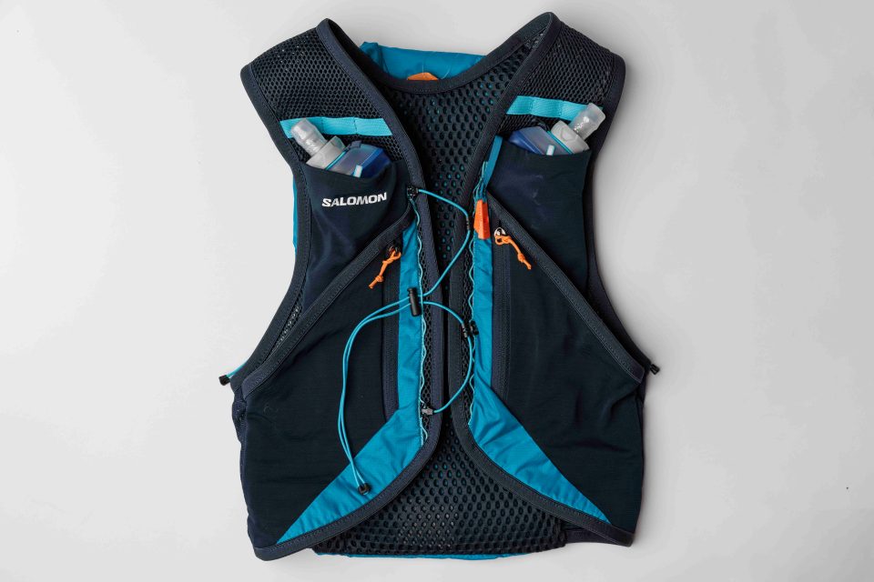 A photo of a person wearing a Salomon Active Skin 12 set, in the color green, with a white and grey backpack. The person is hiking in the wilderness.