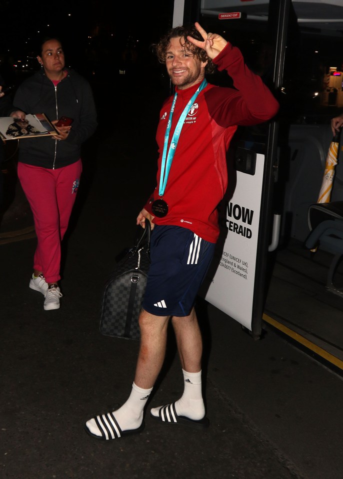 a man wearing a medal around his neck is standing in front of a bus that says now emerald