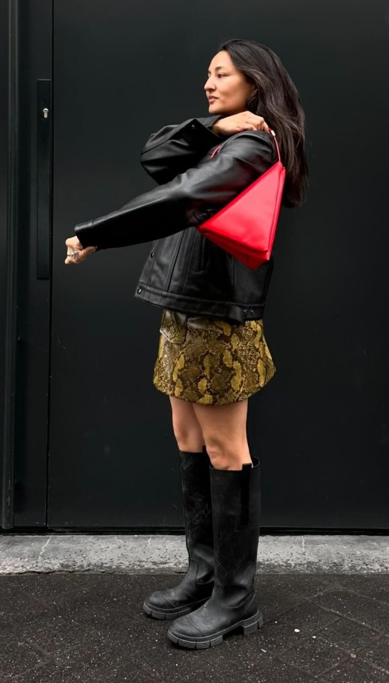 a woman wearing a black jacket and black boots holds a red bag