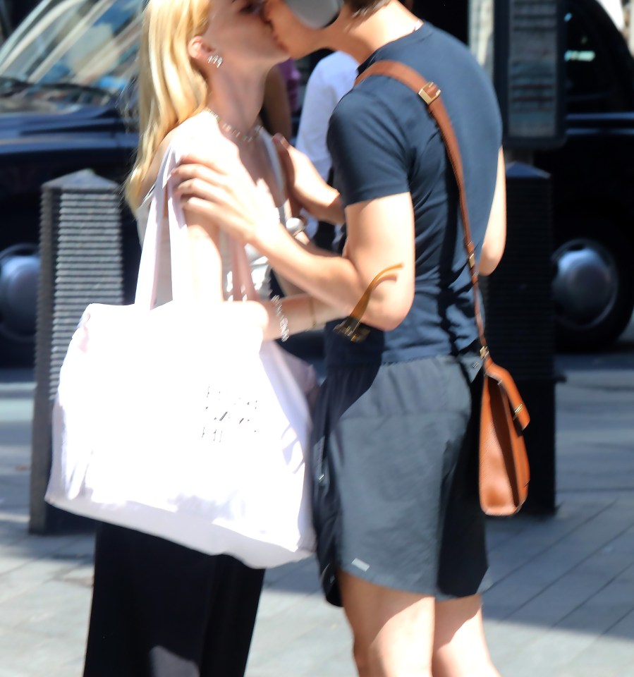 a man and woman are kissing on the street and the woman is carrying a white bag that says ' chanel ' on it