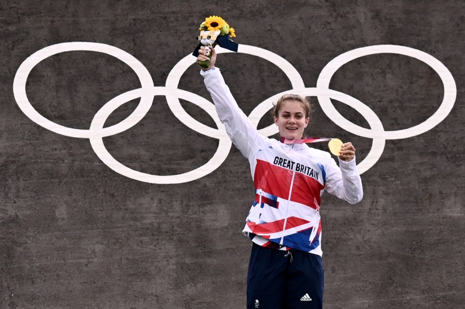 a woman in a great britain jacket holds up her gold medal
