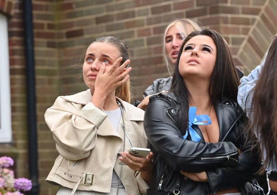 a woman in a leather jacket wipes her eyes with her hand