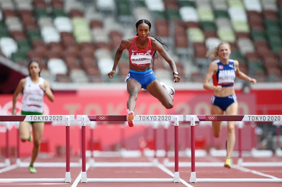 a woman in a usa uniform jumps over hurdles at tokyo 2020