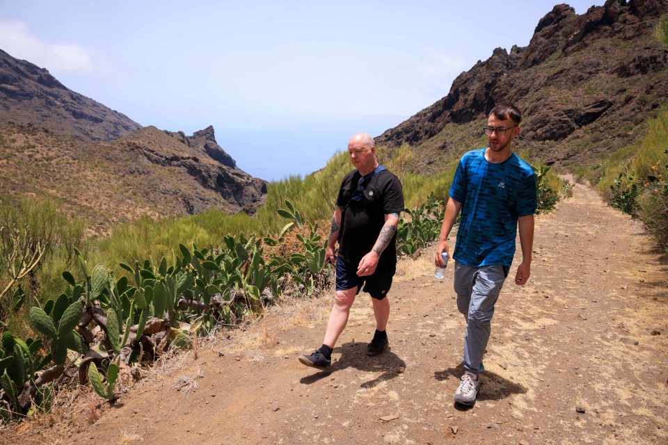 two men are walking down a dirt path in the mountains