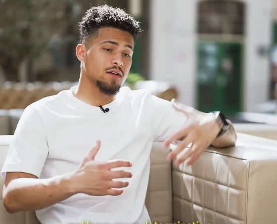 a man in a white shirt is sitting on a couch talking to someone .