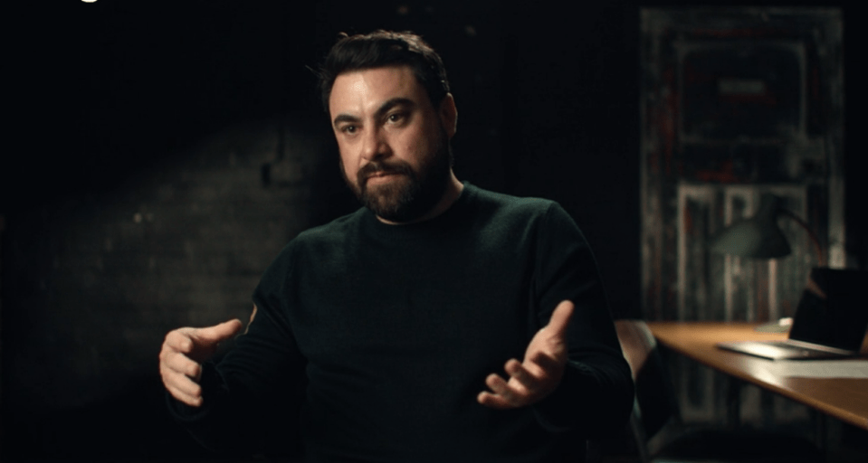 a man with a beard is sitting at a desk with his hands outstretched
