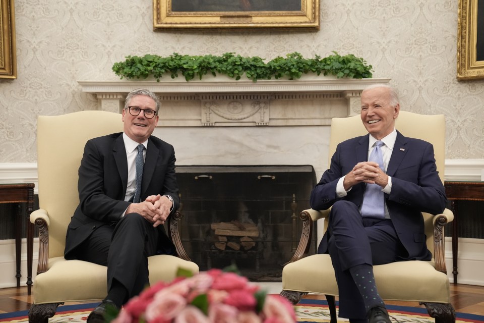 two men sit in chairs in front of a fireplace