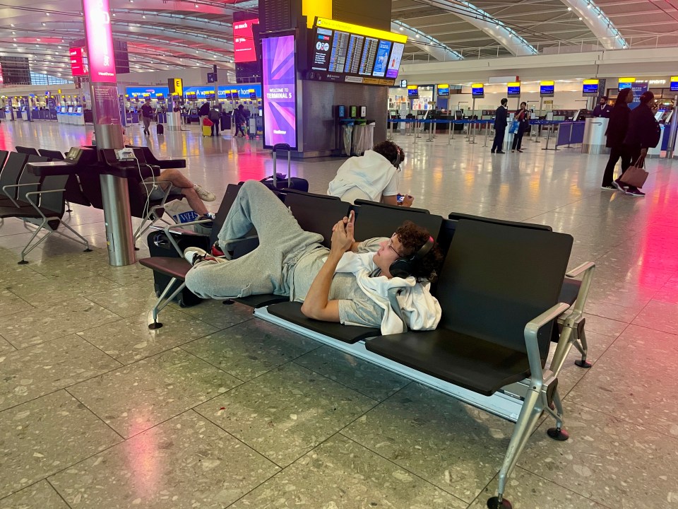 a man laying on a bench in an airport looking at his phone
