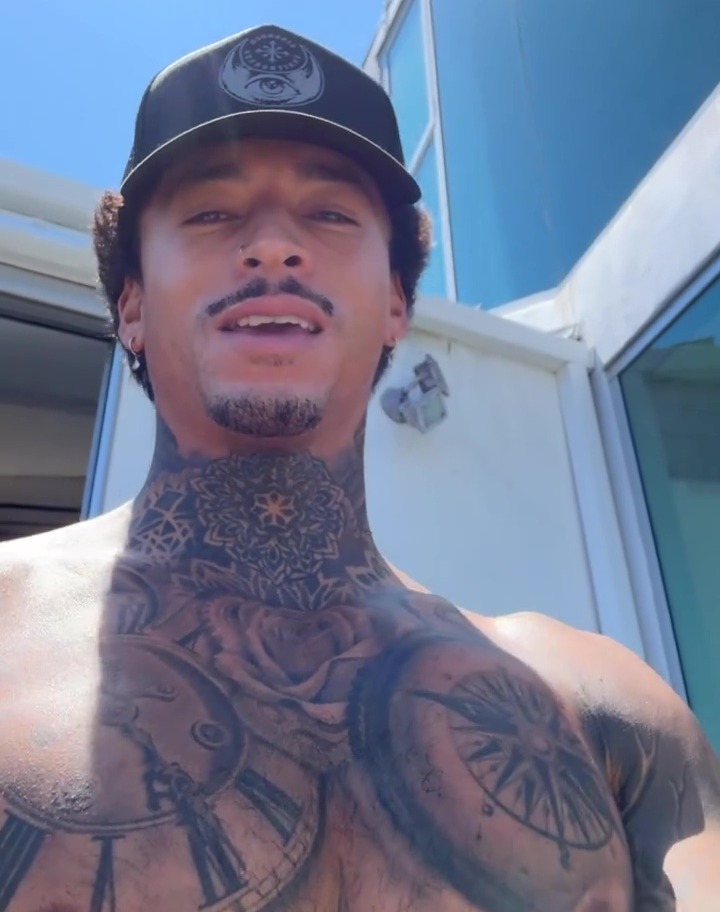 a man with a tattoo on his chest is wearing a black hat