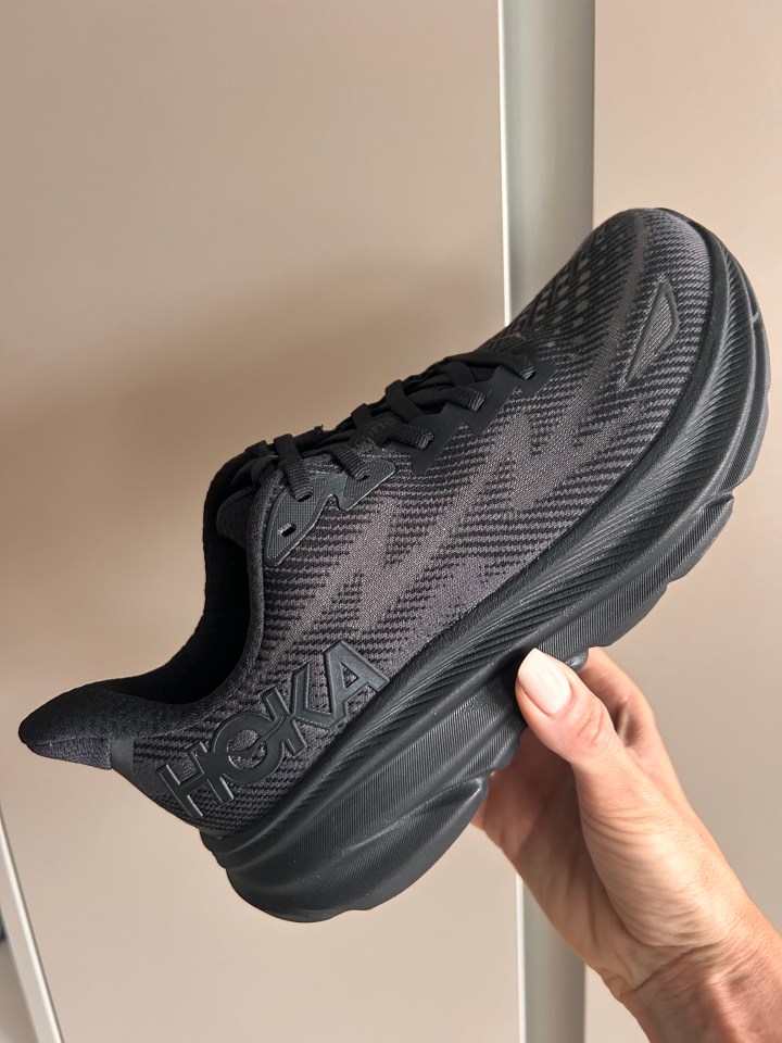 a person is holding a pair of black hoka shoes