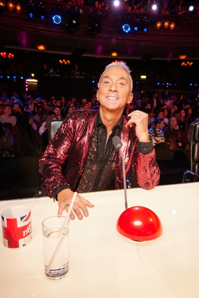 a man in a red sequined jacket sits at a table with a cup that says talent on it