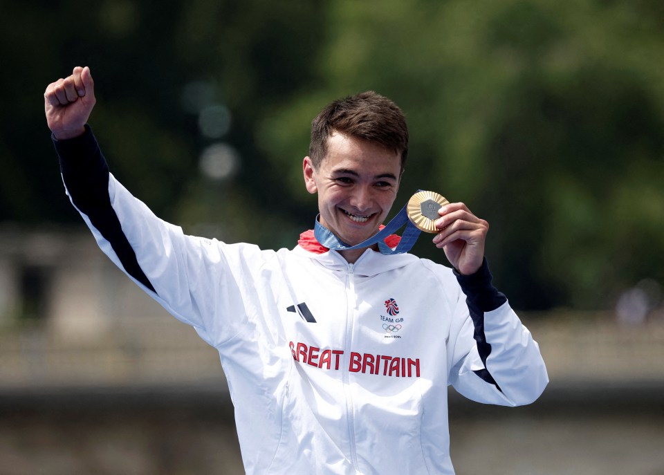 a man wearing a great britain jacket holds up his gold medal