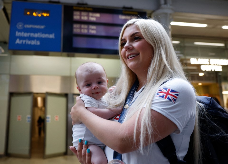 a woman holding a baby in front of a sign that says international arrivals
